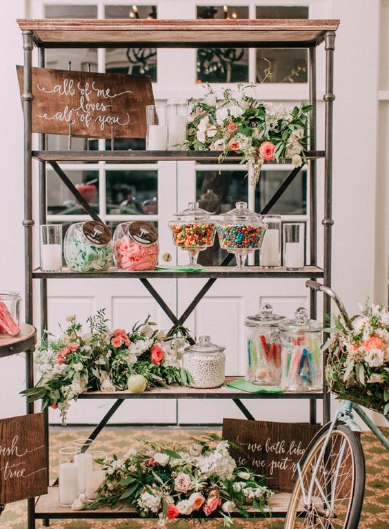 a large rustic shelving unit with greenery, white and pink blooms, signs and lots of candies is a lovely idea for a rustic wedding