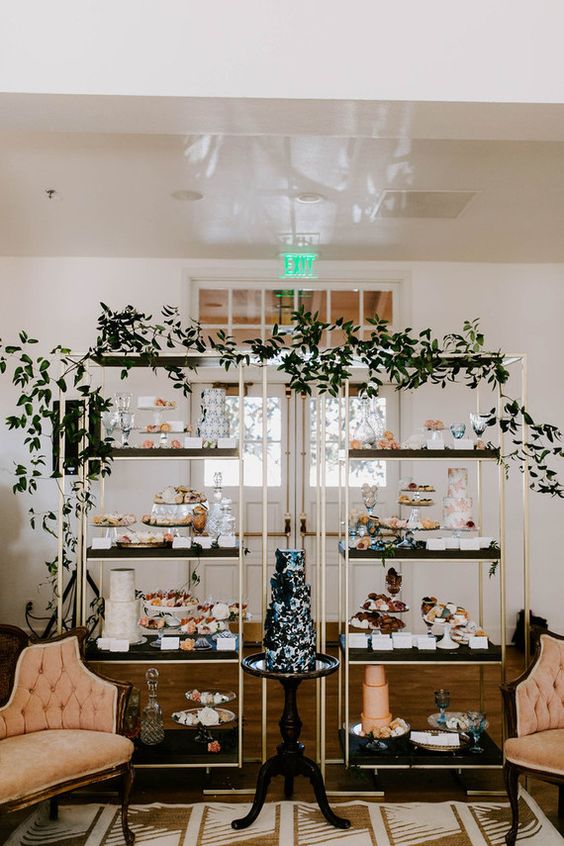 a lovely wedding dessert display composed of two shelves decorated with greenery and with delicious desserts