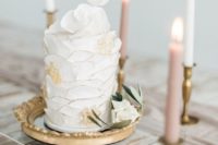 a modern and bright one tier wedding cake with textural white and gold frosting and sugar blooms on top