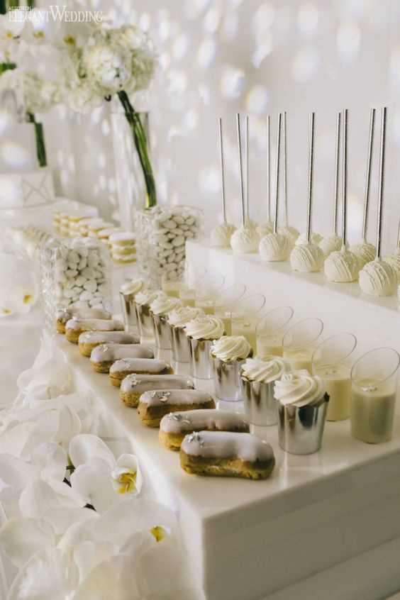 a modern white wedding dessert table with ladders as stands, white blooms is a very sophisticated and chic idea