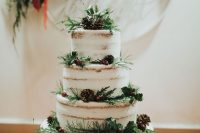 a naked wedding cake with evergreens, berries, pinecones and twigs looks wild and all-natural