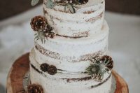 a naked wedding cake with pinecones, berries, thistles and wood slice toppers plus greenery for a winter wedding