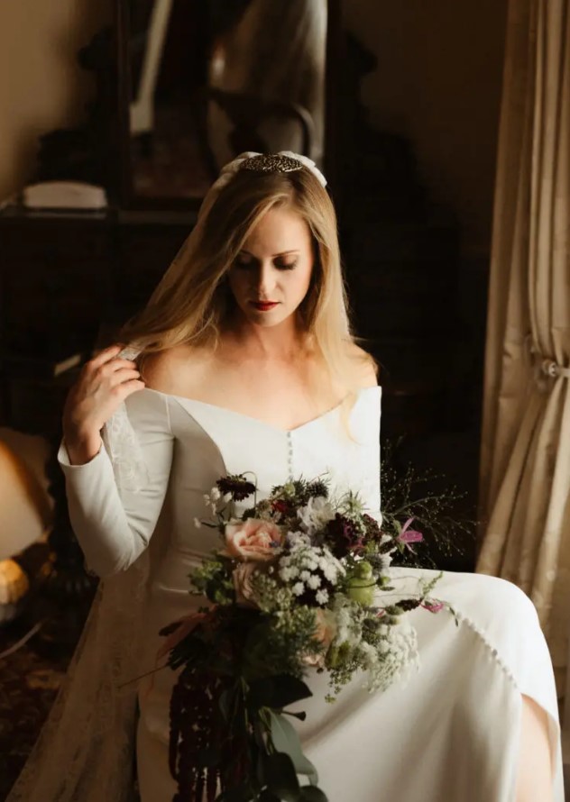 a plain off the shoulder wedding dress with long sleeves and a button row plus a lace veil for a modern fairy tale wedding