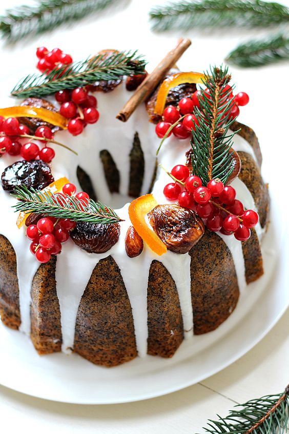 a poppy seed bundt cake with white chocolate drip, cranberries, evergrenes, cinnamon and candied fruit