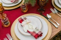 a red table runner and a red plaid napkin, candles, fir branches and elegant cutlery for a Christmas wedding