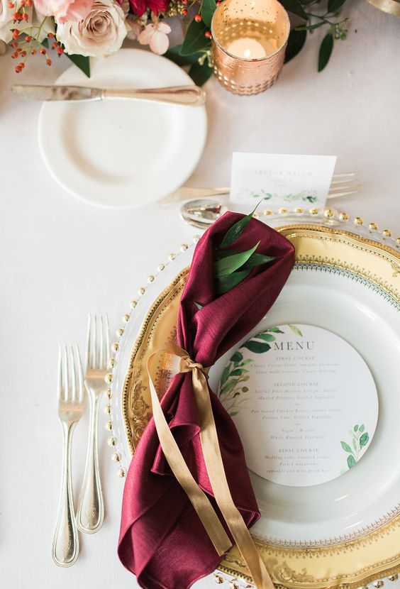 a refined and elegant wedding table setting accented with a marsala apkin and red berries looks perfect for a fall wedding