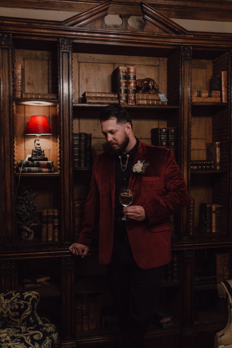 a refined groom's outfit with a black shirt, black pants, a burgundy velvet blazer and a collar chain accessory