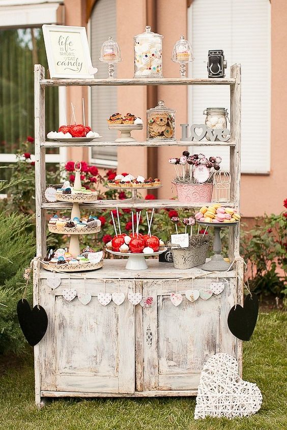 a shabby chic shelving unit with multiple shelves, with candy jars, sweets and printed buntings is a lovely idea for a rustic wedding