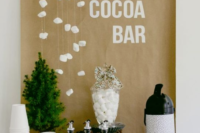 a simple hot cocoa bar with syrups, thermoses, cups and a mini tree plus marshmallows hanging over the bar