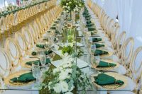 a sophisticated emerald and gold wedding tablescape with a greenery and white runner, emerald napkins, gold placemats and gold-rimmed glasses