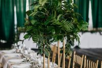 a stylish and chic wedding tablescape with white linens and porcelain, gold clutery and a tall centerpiece with lush greenery