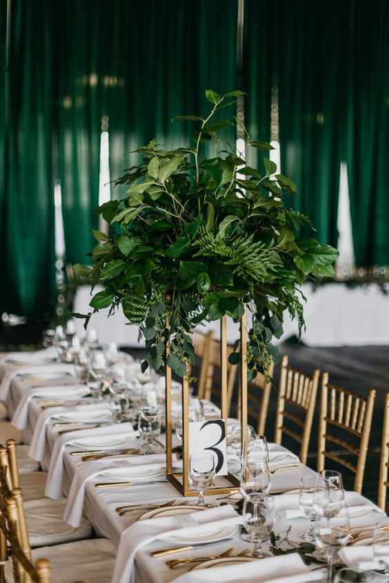 a stylish and chic wedding tablescape with white linens and porcelain, gold clutery and a tall centerpiece with lush greenery