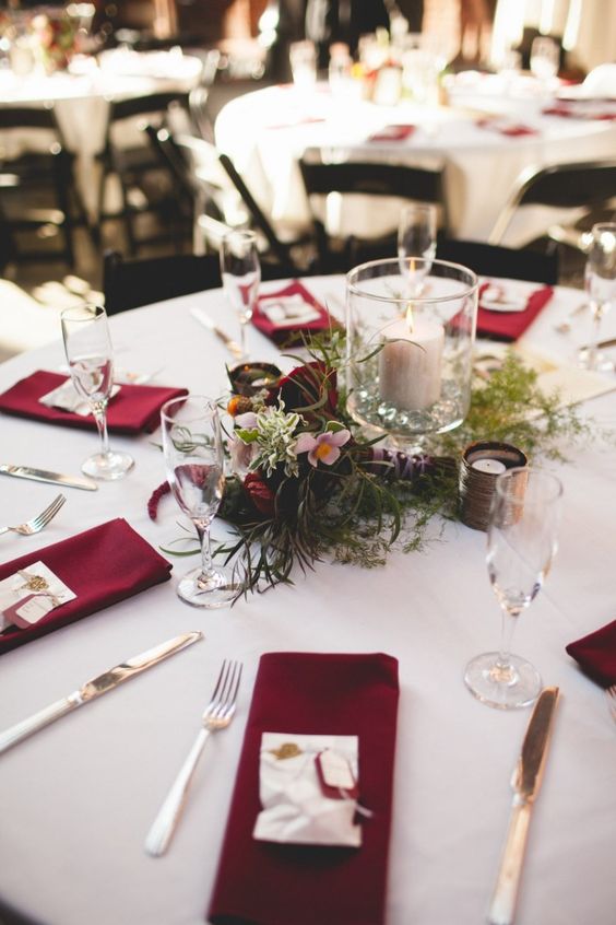 a stylish modern wedding tablescape with marsala napkins, greenery, marsala and pink blooms and candles is very chic