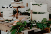 a stylish winter bridal shower dessert table with several white cakes topepd with berries and greenery and decorated with candles