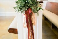 a textural greenery arrangement with blush and burgundy bows and ribbons is a cool decoration for your aisle