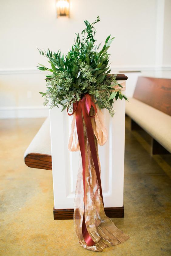 a textural greenery arrangement with blush and burgundy bows and ribbons is a cool decoration for your aisle