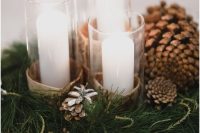 a warming winter wedding centerpiece of evergreens, pinecones, pillar candles and mercury glass candleholders