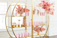 a whimsical gilded shelving unit composed of two parts, decorated with pink blooms and delicious sweets on display