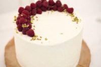 a white buttercream one tier wedding cake topped with pistachios and raspberries as a semi-circle for a chic wedding