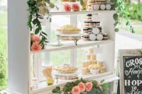 a white shelving unit with greenery and peachy pink blooms and with lots of desserts is a lovely idea for a refined wedding