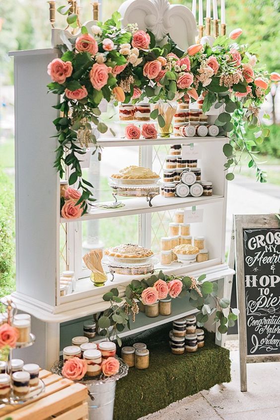 a white shelving unit with greenery and peachy pink blooms and with lots of desserts is a lovely idea for a refined wedding