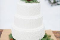 a white textural wedding cake with faux fur and pinecones served on a platform of evergreens and pinecones
