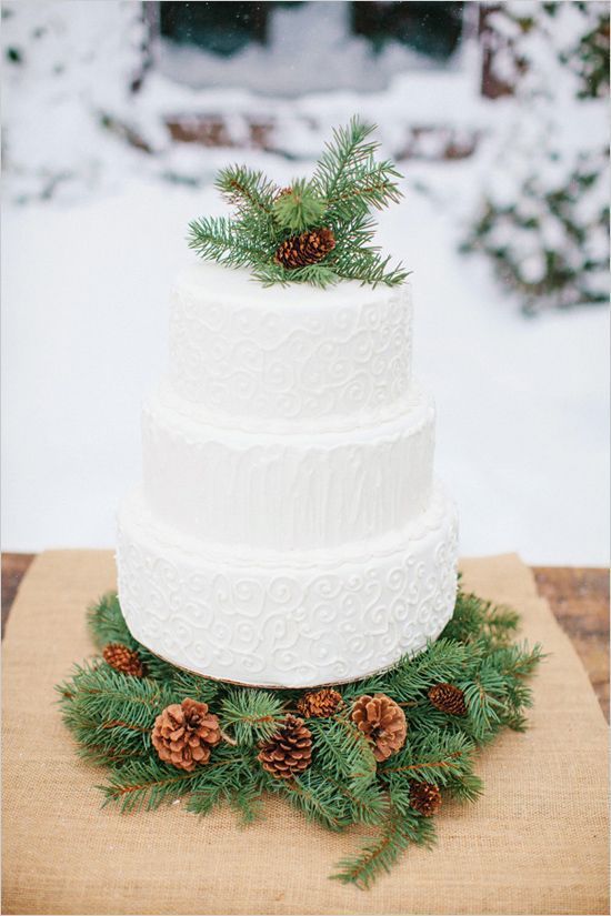 a white textural wedding cake with faux fur and pinecones served on a platform of evergreens and pinecones