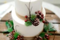 a white wedding cake decorated with burlap, berries, pinecones, twigs and evergreens for a winter wedding