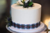 a white wedding cake with a tartan ribbon, thistles and white blooms on top is a stylish and bold idea