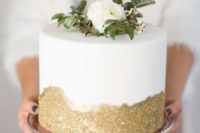 a white wedding cake with gold glitter and fresh greenery and blooms is a cool idea for a modern wedding