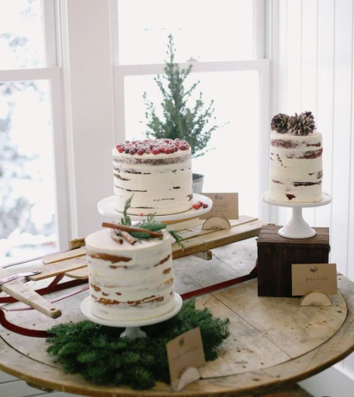 a winter bridal shower dessert table with three naked cakes topped with berries, cinnamon and pinecones