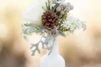 a winter wedding centerpiece of a white bottles with berries, pale greenery, white roses is a romantic decoration