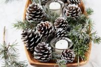 a winter wedding centerpiece of a wooden bowl with evergreens, snowy pinecones and pillar candles is lovely