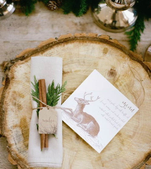 a wood slice instead of a usual placemat, a deer printed menu and cinnamon sticks and evergreens to mark the place setting