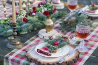 an elegant Christmas wedding tablescape with a colorful plaid runner, gold candles and vases, fir branches and cranberries