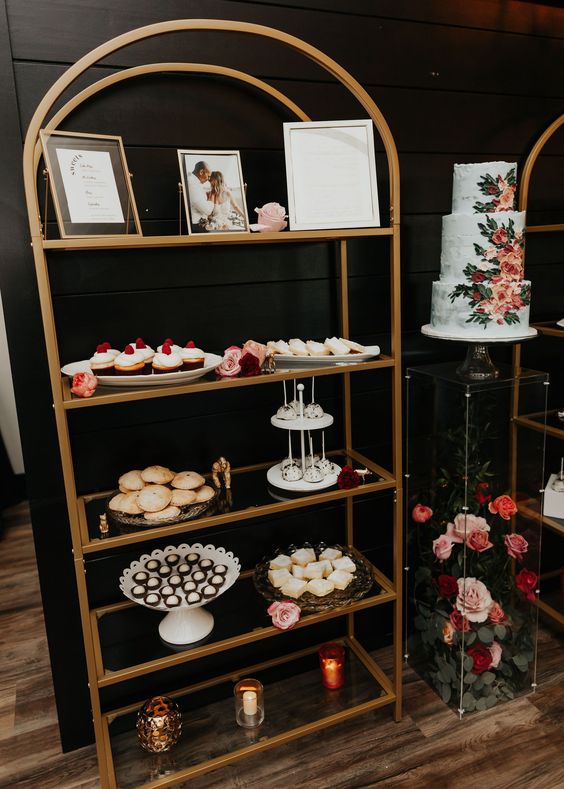 an elegant arched brass shelving unit with photos and lots of desserts, candles and blooms is a stylish idea for a modern wedding