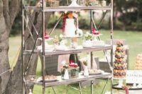 an elegant vintage shelving unit with lots of desserts, grenery and bright blooms is a stylish idea for a garden wedding