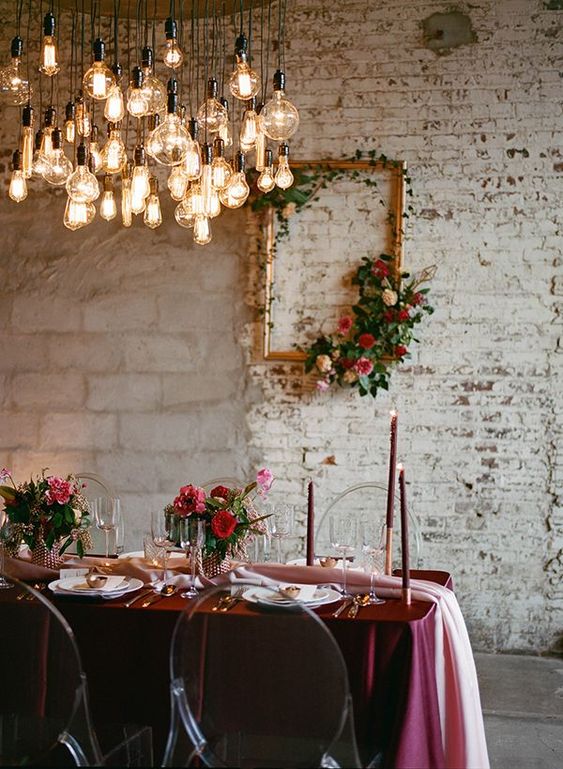 an exquisite wedding tablescape with a marsala tablecloth, candles, red and pink blooms and gold cutlery is amazing