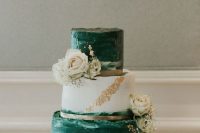 an eye-catchy wedding cake with green brushstroke tiers, a white and gold glitter one, white roses and greenery