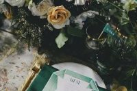 emerald napkins, drink stirrers, gold cutlery and gold rim glasses with a lush floral centerpiece
