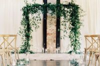 greenery and floating candles in tall vases and a greenery arch with candles create a very chic and natural ceremony space