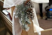 snowy evergreens, snowy pinecones and a large bow are traditional decorations for a winter wedding aisle