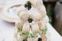 white macarons served on a stand with greenery and pinecones is a stylish winter-inspired idea