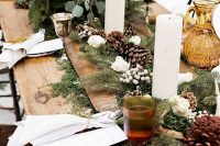 winter wedding table decor with evergreens, pinecones, white roses, berries, pillar candles and greenery
