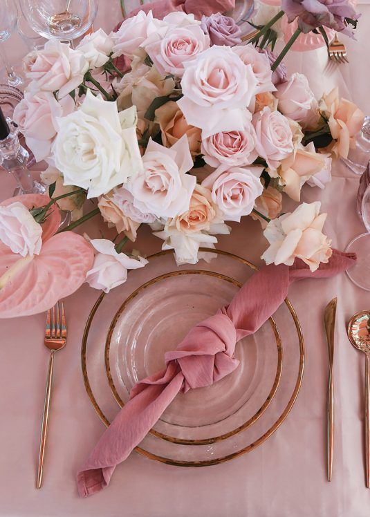a beautiful Valentine's Day wedding table in pink, with gold rimmed plates, blush and pink blooms and a pink napkin