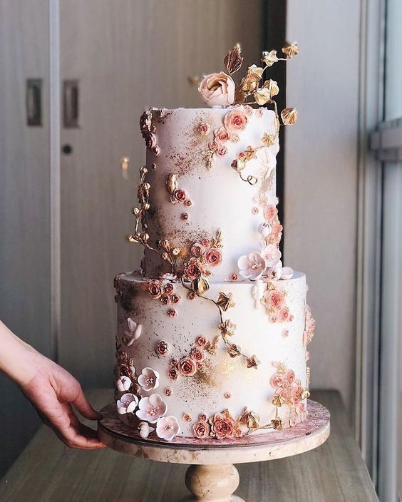 a beautiful blush wedding cake fully covered with pink and blush sugar blooms and gold blooming branches is wow