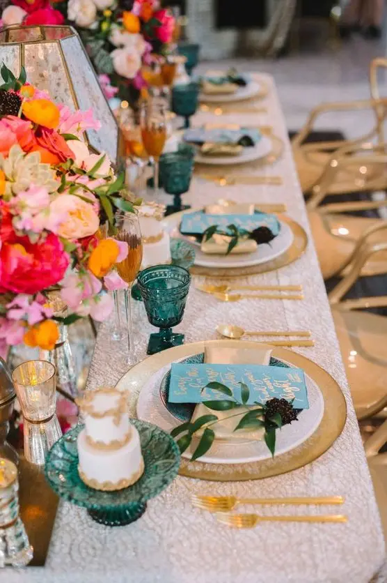 a beautiful summer wedding tablescape with a printed tablecloth, gold chargers and cutlery, bright blooms and candleholders