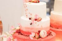 a beautiful white, pink and red wedding cake decorated with pink blooms, strawberries and macarons for a Valentine wedding
