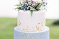 a blue marble and white wedding cake with gold foil and white and blue blooms and berries on top plus some foliage