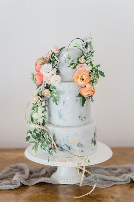 a blue marble wedding cake with gold foil, white, coral and orange blooms, greenery and ribbons for a spring or summer wedding